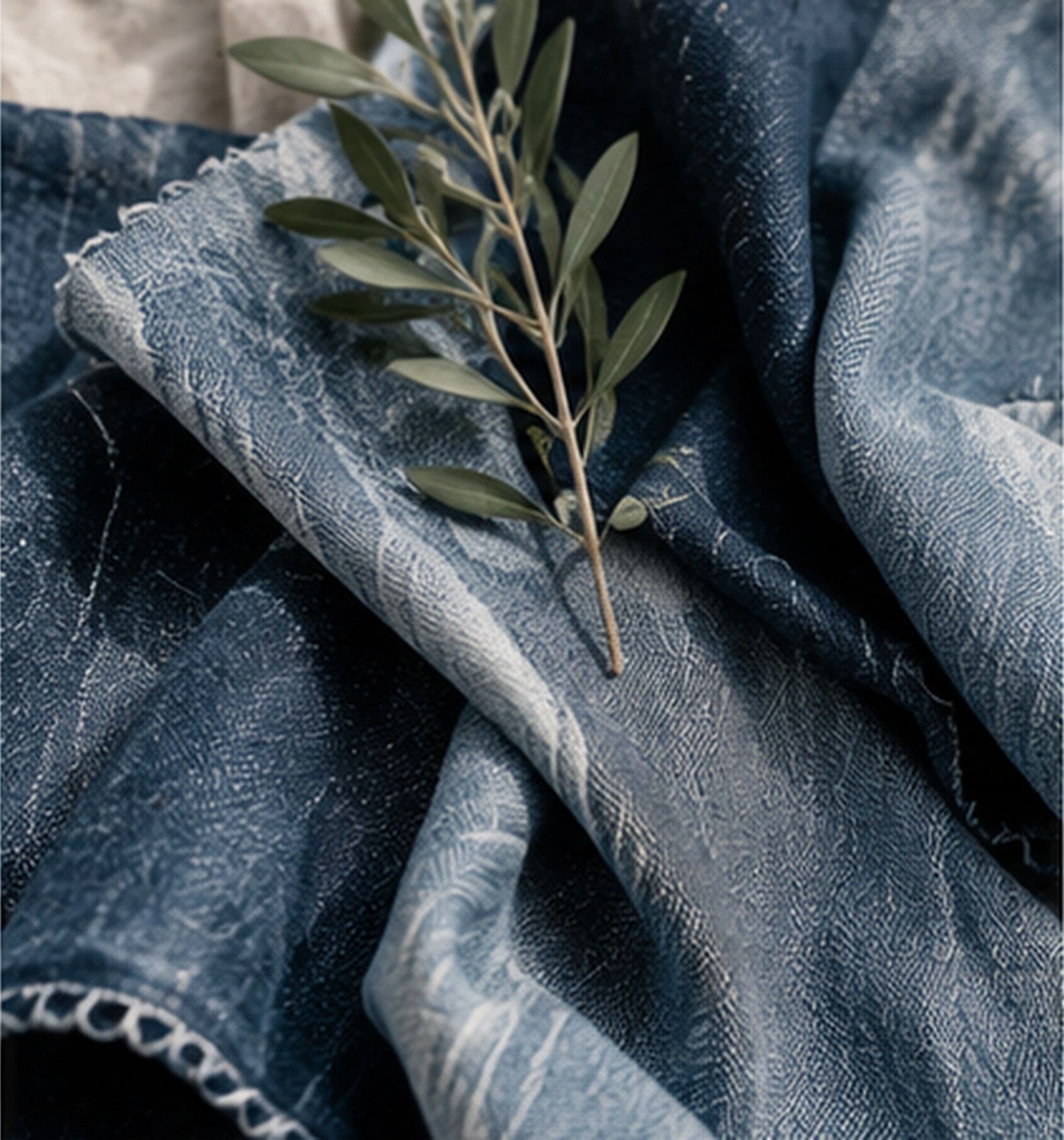 A sprig of olive leaves resting on folded indigo denim fabric with a textured weave.